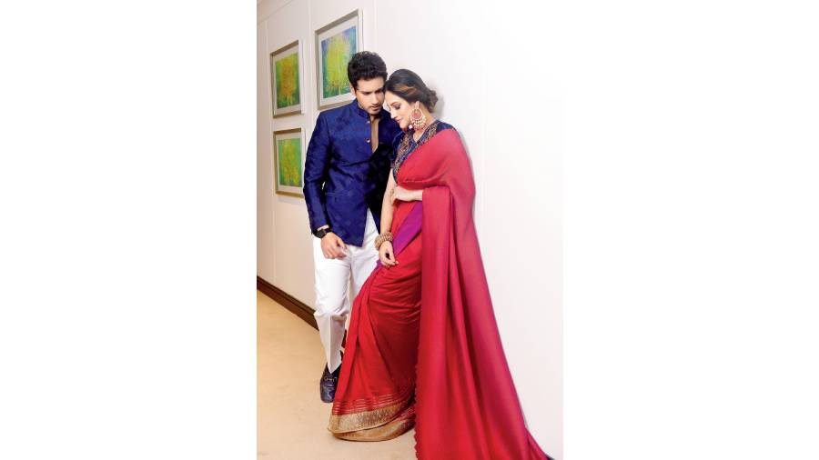 Nusrat looks stunning in this two-tone pleated sari by Kiran Uttam Ghosh (available at 85 Lansdowne), contrasted with a navy velvet embroidered blouse by Karuna Khaitan (available at 85 Lansdowne). The eyes are dramatic blue-smokey and the lips subtle. The messy bun and bold jewellery add to the allure. Yash looks red-carpet ready in an embroidered fine cotton silk bandhgala by Khanijo (available at Dapper, 10A&B Woodburn Park).