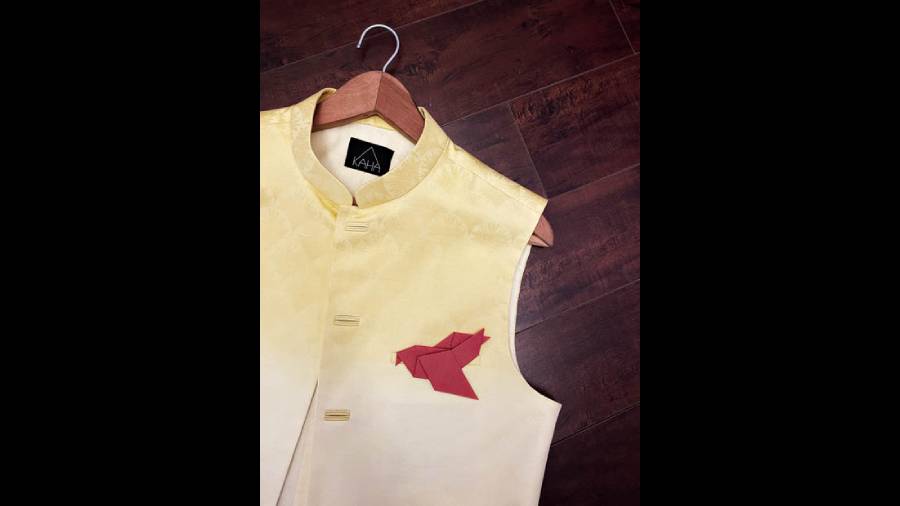 Another ombre light golden and white pure linen jacquard half jacket to wear atop that favourite dark red or maroon kurta of yours, this one stands out for the bird-shaped origami pocket square made of paper folding. Complete the look with red churidar pants and brown sandals.