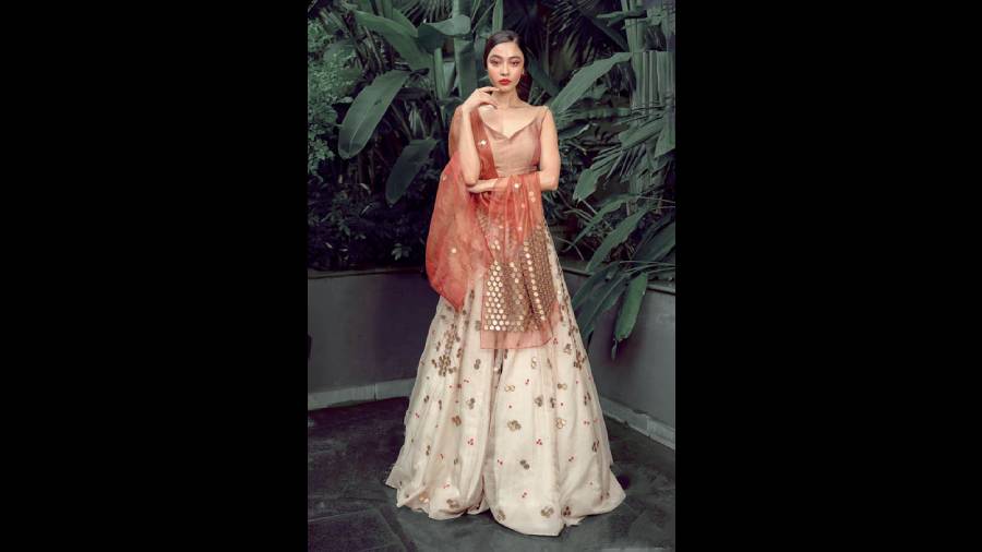 Diti Saha channelled a simple glam look in a traditional lehnga designed with a contemporary touch. The ox-red and ecru lehnga with an attached drape in organza is designed with golden honeycomb motifs all over and sprinkled with red embroidery work. Bold lips accentuate the metallic shades of the outfits.