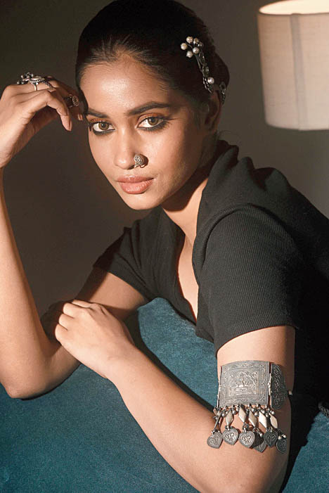 A silver choker is quite a common jewellery item in one’s casket. Use it as a statement armlet and grab all eyes! Designed with motifs from tribal culture, this choker from Karishmaz with an adjustable tassel cord does well as an armlet too. A brooch used as a hair accessory completes the look.