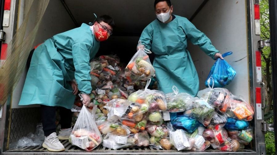 Workers wearing protective gear sort bags of vegetables and groceries on a truck to distribute them to residents at a residential compound, in Shanghai on Tuesday.