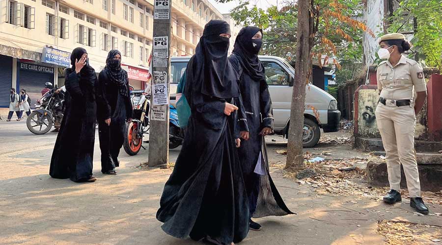 Hijab-wearing students arrive to attend classes as a policewoman stands guard outside a government girls school after the recent hijab ban, in Udupi town in Karnataka