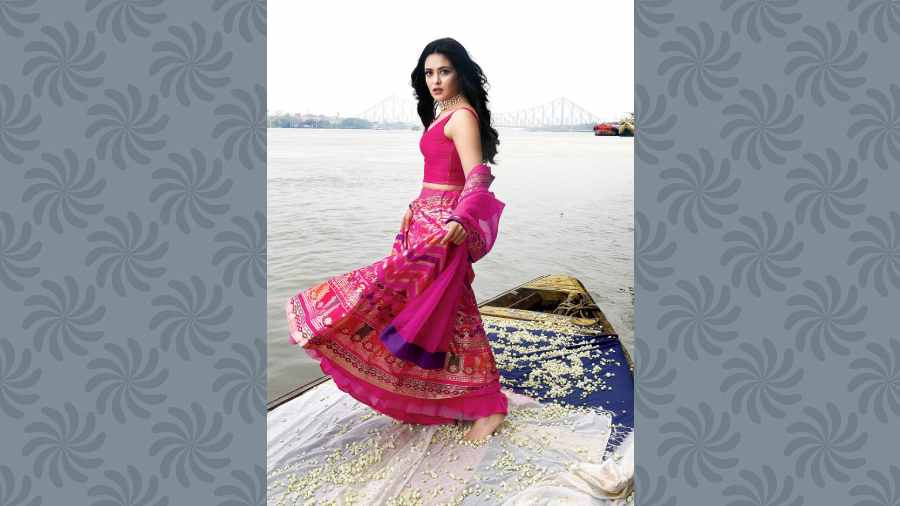 A colourful and super glam festive evening or occasion-wear look, the chevron-patterned bright pink lehnga is detailed with seven different colours and intricate zari detailing. A mix of floral and geometric design makes it summery and contemporary in its appeal, paired with a sheer organza dupatta.