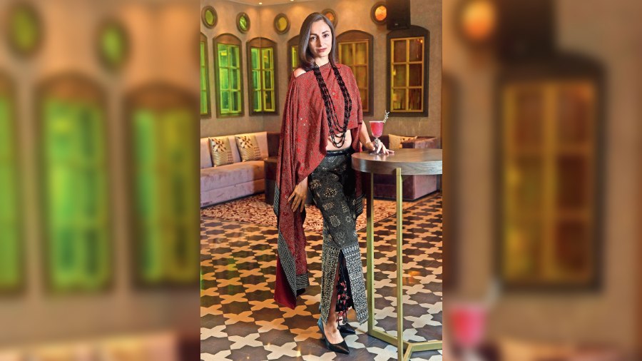 Iryna sports a red-and-black co-ord set with a “red flowy cape intricately embroidered in a traditional design”. Accessories have been kept simple with strands of beads on the neck. The Floral Jamun drink in her hand fits the mood just right.