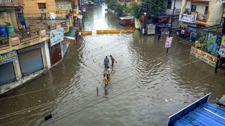 Locals wade through a waterlogged street following incessant monsoon rains in Indore on Wednesday