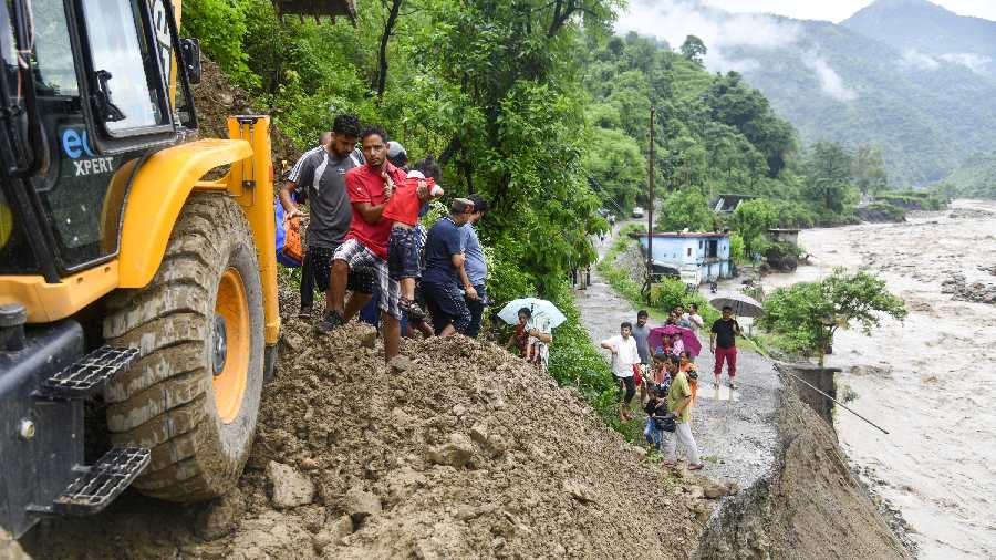 People walk on debris over a road, after a series of cloudbursts hit different parts of Uttarakhand