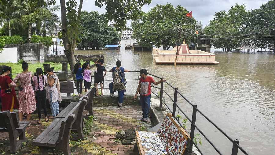 People standing on an elevated ground look at a partially submerged temple in a flood affected area in Surat