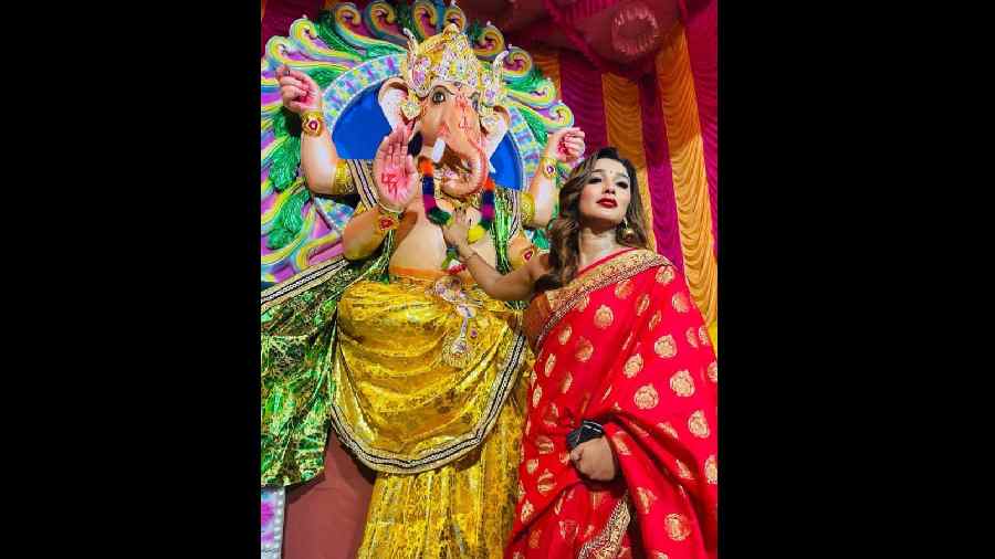 Bengali actress Sayantike Banerjee, dressed in a red saree poses in front of Ganesh idol