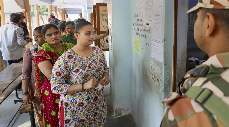 A security person stands guard as people stand in a queue to cast their votes for the first phase of Gujarat Assembly elections, in Surendranagar on Thursday.