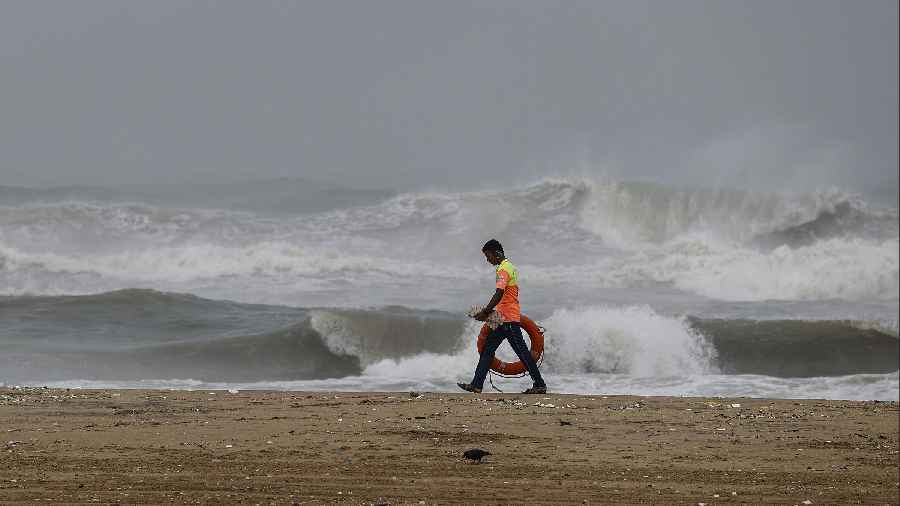 A lifegaurd walks along the sea-shore as waves crash onto the shore ahead of the landfall of cyclonic storm Mandous, in Chennai