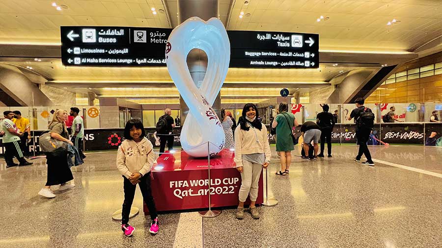 Myra and Ayesha strike a pose on arrival at the Doha international airport. The swooping curves of the official logo of the FIFA World Cup 2022 in the background represent desert dunes, and the unbroken loop depicts both the number eight – representing the tournament’s host stadiums – and the infinity symbol, reflecting the event’s interconnected nature, fusing tradition with modernity