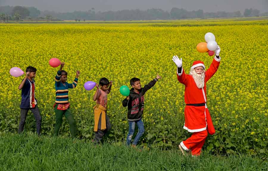 Children have fun with a man dressed as Santa Claus in a farm field in Nadia on Saturday