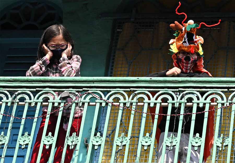 Young residents of Tiretti Bazar — some in Covid masks, others in more decorative gear — look on as the procession passes below