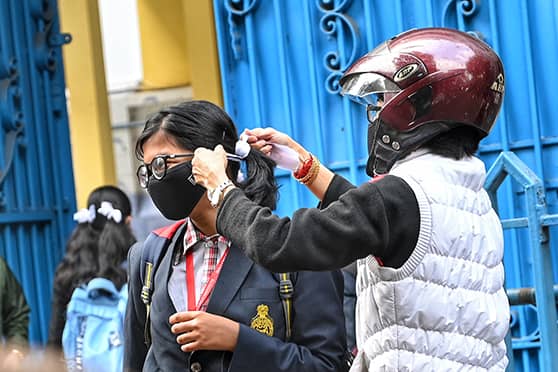 A parent ties her ward’s hair, ensuring her mask is in place, before she enters Holy Child Girls High School on reopening day. 