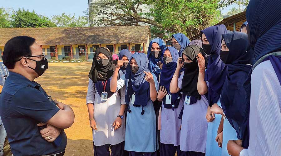 A faculty member talks with the students wearing hijab, after the school authorities denied them entry for wearing a hijab or scarf, in Kundapura of Udupi district, Saturday, Feb 5, 2022. 