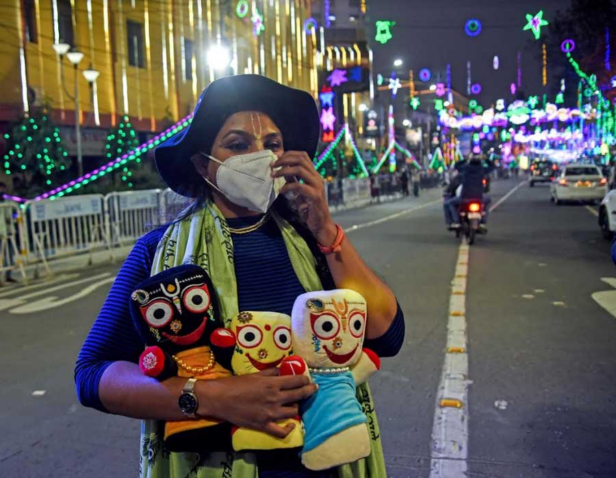 EVENING JAUNT: A masked Vaishnavite walks down a brightly illuminated Park Street in central Kolkata, holding the wooden idols of Lord Jagannath, Devi Subhadra and Lord Balabhadra in woollies in his arms on Thursday, December 30. 