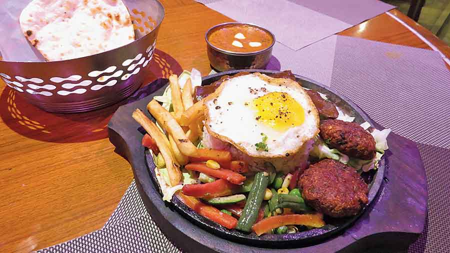 Tandoori Jhinga and Prawn Nuggets served on a sizzler with the glass and teakwood decor of the seating area of Orko’ss in the backdrop. 