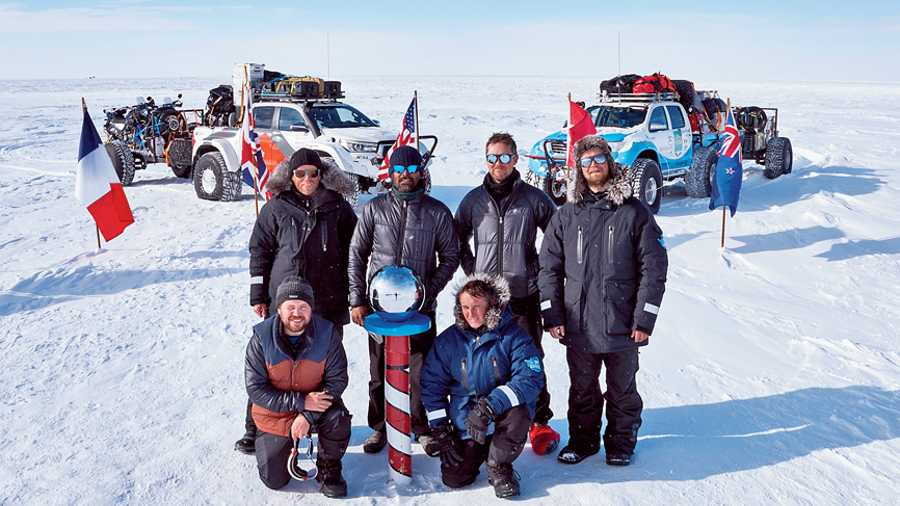 The six-member 90°South team at the pole marked by a red and white post