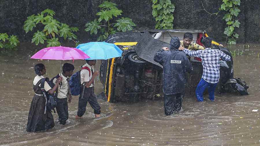 Students walk past as others try to repair an auto-rickshaw on a flooded road amid heavy monsoon rains