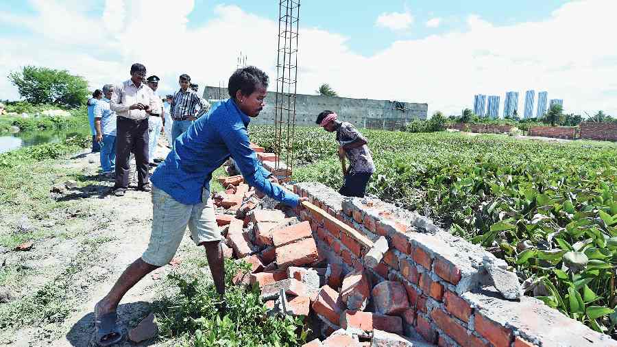 A wall that was being built around a water body in the East Kolkata Wetlands being pulled down on Thursday