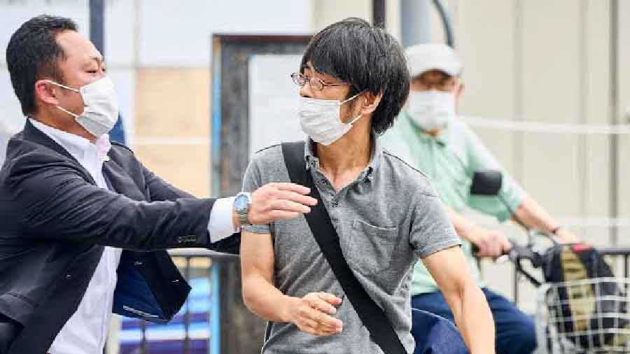 Tetsuya Yamagami (R), with his homemade gun slung across his shoulder, being detained by a police officer after latter fired gunshots at Shinzo Abe 