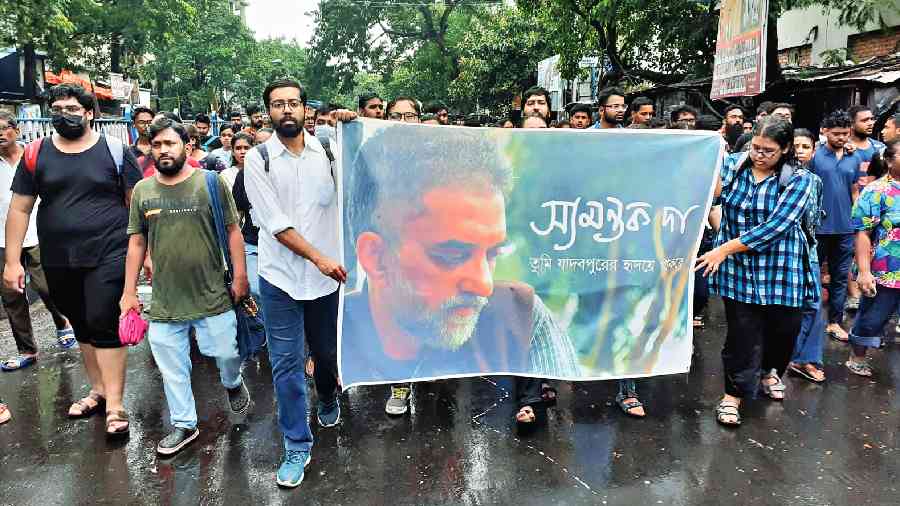 Students hold a poster that has an image of Das with a message saying ‘You will remain in the heart of Jadavpur’