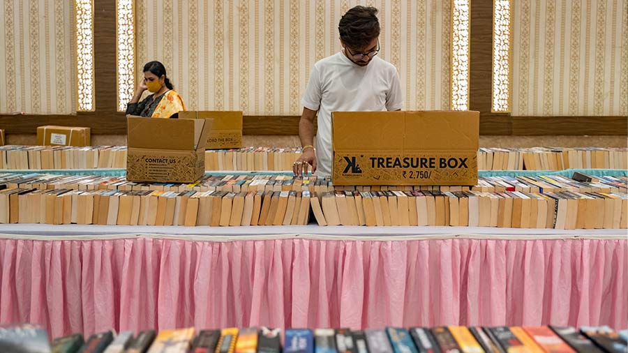 Visitors at the fair browse through books stacked on tables and shelves.