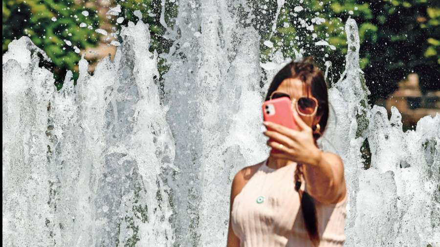A woman clicking a selfie in front of a fountain. On the app BeReal, first a photograph of what is in front of the camera gets captured and then a selfie of the person clicking the other shot.