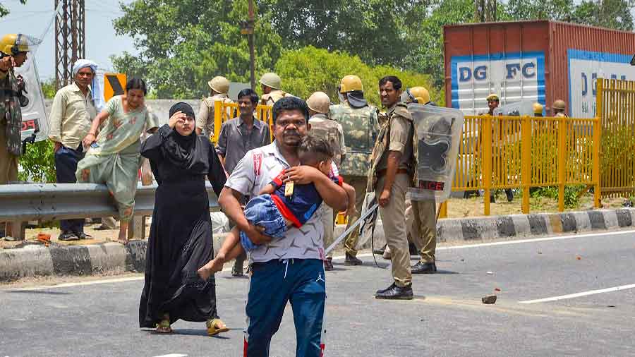 A man carrying his child and family head for a safer place during a clash between security personnel and people protesting against Centres Agnipath scheme, on Agra-Delhi National Highway in Mathura