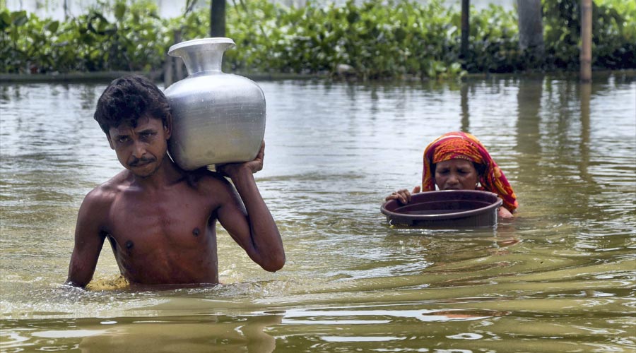 Villagers carry potable water in containers as they wade through a flooded area at Nilambazar village, in Karimganj district.