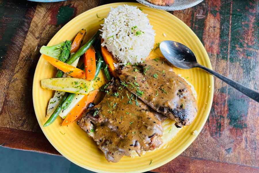 GRILLED CHICKEN FROM CAFE NA-RU-MEG: Perfectly grilled chicken breasts served on a bed of creamy mashed potatoes is comfort food for the soul. The classic brown sauce and sauteed veggies make the dish come together at this Raja Basanta Roy Road cafe. Pro tip: Ask for the herbed rice