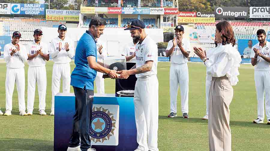 Rahul Dravid presents Virat Kohli his 100th Test cap on  Friday, as Kohli’s wife Anushka Sharma (right) and other team members look on.