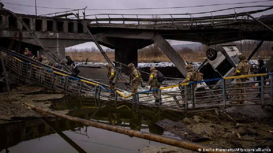 Ukrainian soldiers cross a heavily damaged footbridge on the outskirts of Kyiv