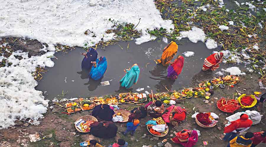 Devotees offer prayers as toxic foam floats on the Yamuna river during the Chhath Puja in New Delhi. 