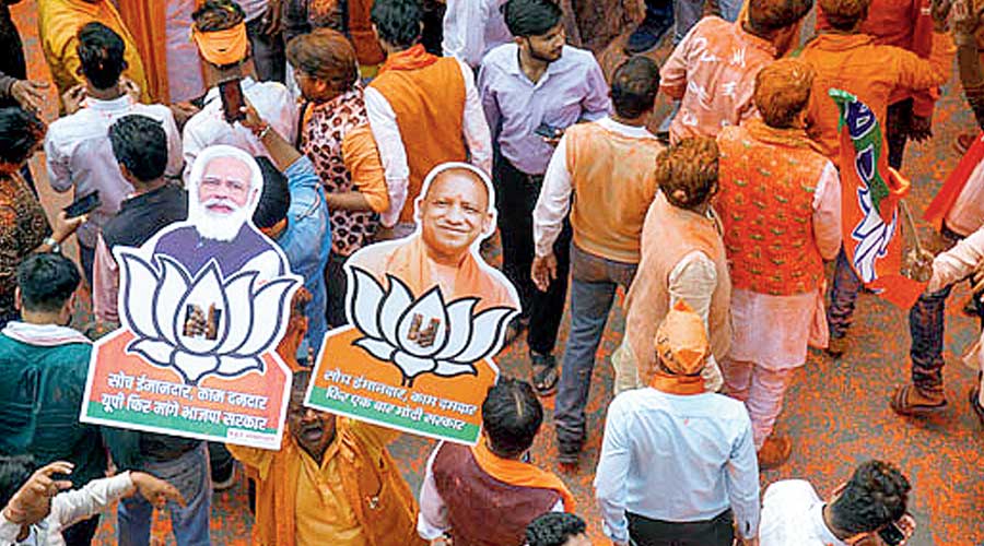 BJP supporters holding cutouts of Prime Minister Narendra Modi and UP Chief Minister Yogi Adityanath, celebrate with colours, as the party heads to a landslide victory in UP Assembly elections, at the party office, in Lucknow, Thursday, March 10, 2022.
