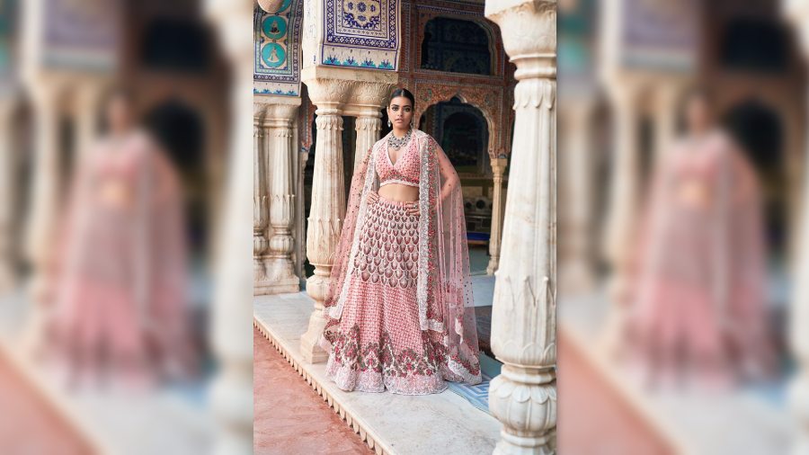 The flamingo peach tulle lehnga has Caviar pearls and Swiss embroidery and is teamed with a halter blouse and matching tulle dupatta.