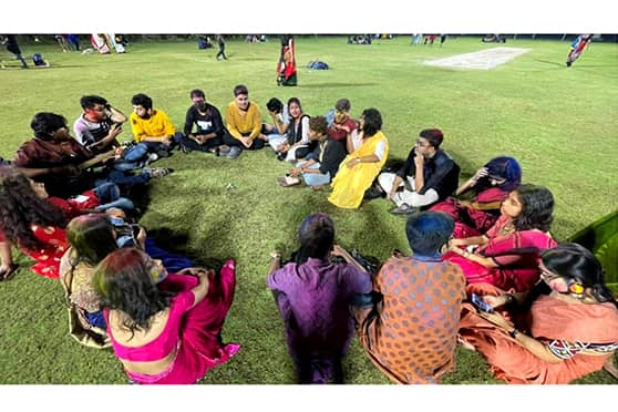 Students sit on the field in groups post-Holi celebrations.  
