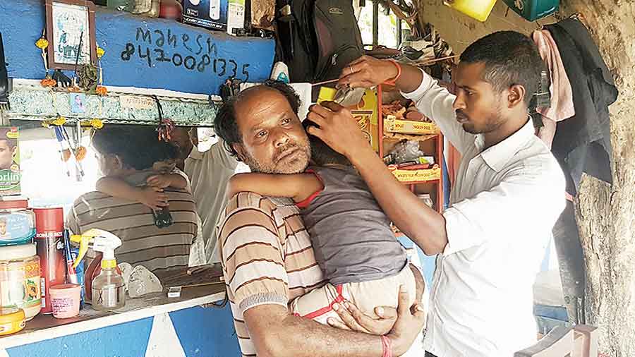 Pawan Kumar, a barber who sits on the footpath near Tank 12, trims  a child’s hair. 