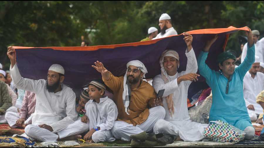 Muslims cover themselves with a plastic sheet as they prepare to offer prayers amid rains