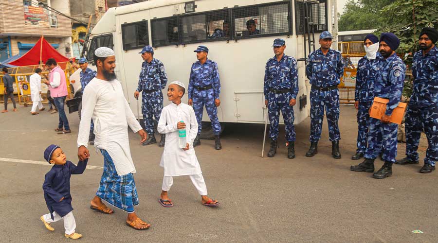 RAF jawans stand guard as a Muslim man walks with children on Eid-al-Fitr, in violence-hit Jahangirpuri area in New Delhi on Tuesday.