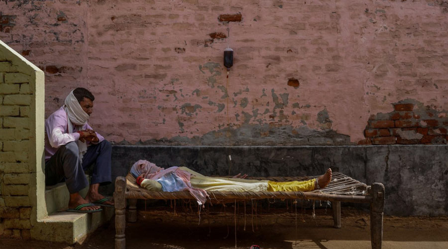 A man sits next to his wife, who was suffering from a high fever, as she intravenously receives rehydration fluid at a makeshift clinic during a surge of the coronavirus disease in Parsaul village located in the northern state of Uttar Pradesh, India, May 22, 2021. (Adnan Abidi)