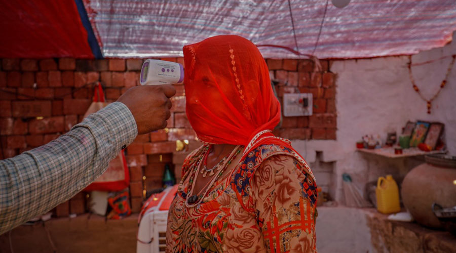 A healthcare worker checks the temperature of a woman inside her hut during a coronavirus disease vaccination drive for workers at a brick kiln in Kavitha village on the outskirts of Ahmedabad, India, April 8, 2021. (Amit Dave)