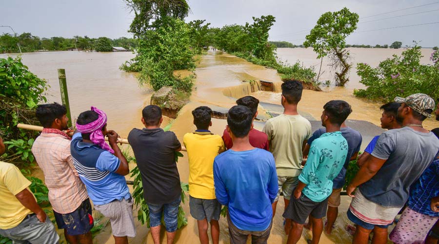 Villagers look at a damaged road after heavy rainfall, at Kampur village in Nagaon district
