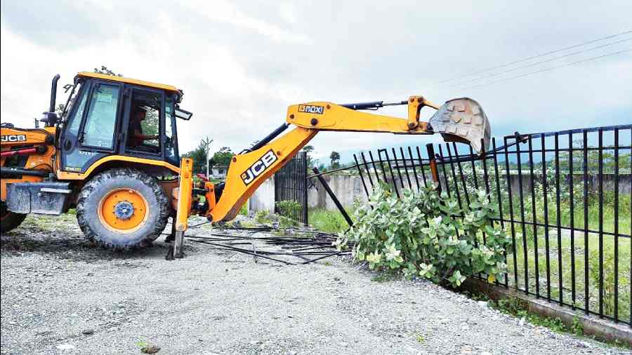 An excavator pulls down the wall of a government plot in Jaigaon on Saturday. 