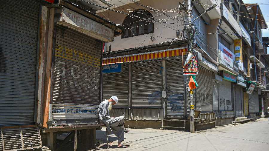man sits outside a closed shop during a strike in support of JKLF chief Yasin Malik, in Srinagar