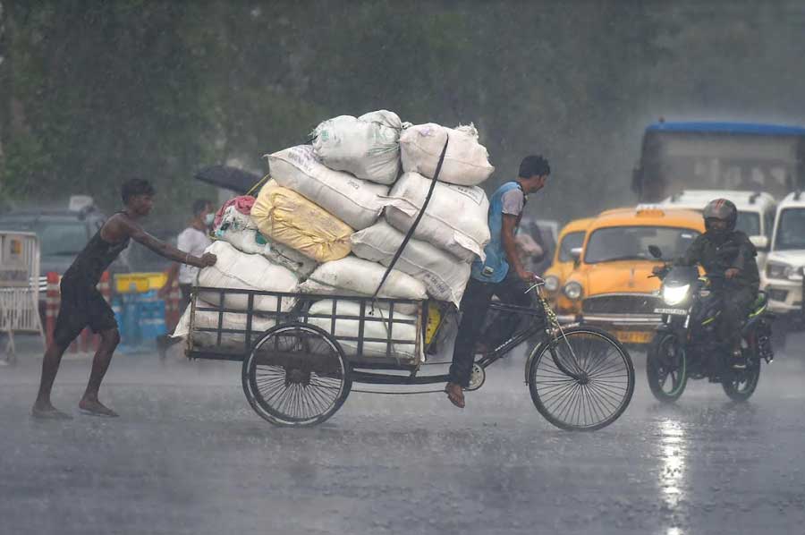 Porters carry goods on a van-rickshaw during an afternoon shower on Thursday