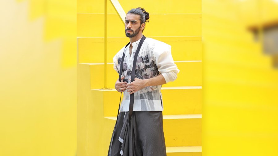 Keeping up with the popular trends of the season, the silk-Chanderi short kurta layered with a frayed silk-textured tulle overshirt and tie-up collar is paired with a striped Chanderi pre-draped dhoti designed with reflective tape detailing.