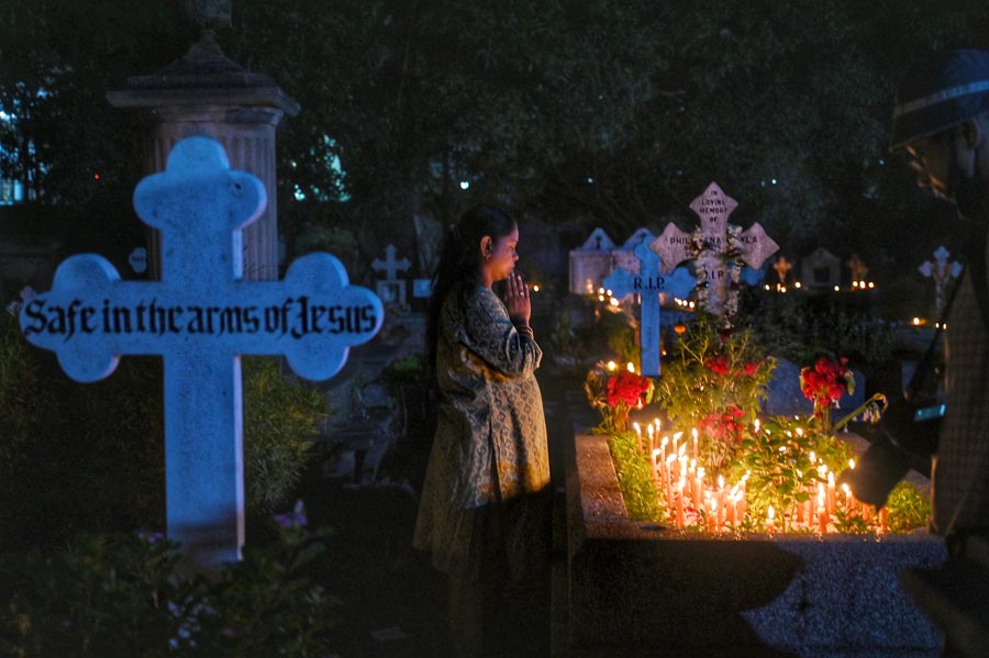 A woman prays in front of a grave. It is one of the busiest days for the cemetery staff as family members follow up on the annual upkeep of the tombs and graves 