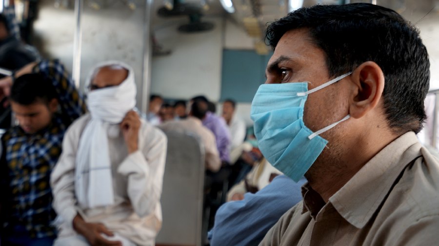 Passengers wearing facemasks ride a train across the Yamuna river