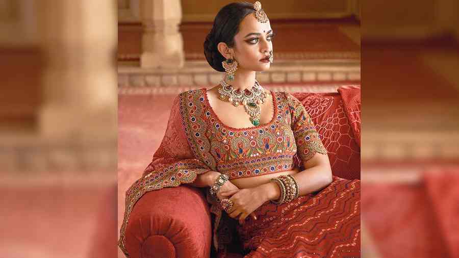 Set in 22k gold, this polki bridal set is an elegant piece for adding to your wedding casket. The polki necklace and earrings are studded with emeralds, tourmalines and pearls, detailed with Rajasthani borla. The polki nath designed with red cabochon, pearls and red ruby beads; polki and emerald-studded bracelet and stack of polki pacheli and kada complete the look